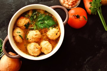 Soup with meatballs and vegetables on a dark background, top view. Vegetable soup with chicken meat and beans, ingredients on the table