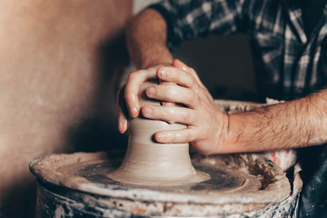 Man forms a white clay product on a pottery wheel 