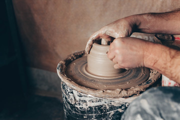 Man forms a white clay product on a pottery wheel side view