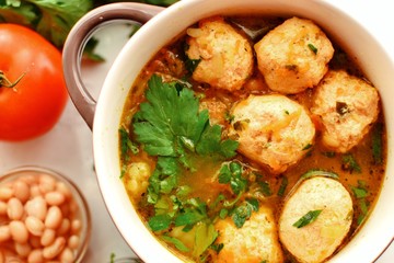 Soup with meatballs and vegetables on a white table background, top view. Vegetable soup with chicken and beans.