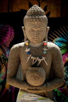 Smiling Buddha statue outdoor wearing a necklace in backlit sunlight and colourful dark background