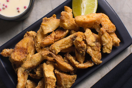 Fried Tilapia strips in a black platter with rose pepper sauce in background seen from above with half light