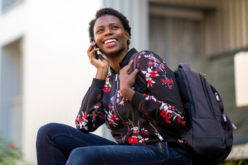 happy young african woman sitting with bag talking with mobile phone