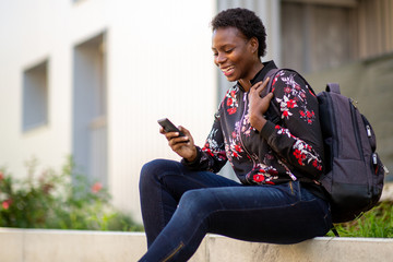 Obraz premium Side happy young african woman sitting with bag looking at mobile phone