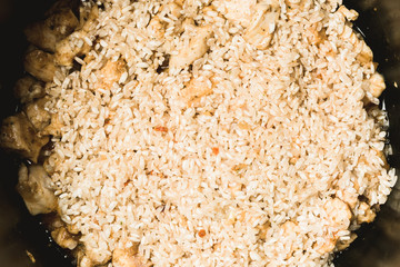 Laying ordinary rice and chicken pieces for making pilaf in slow cooker.
