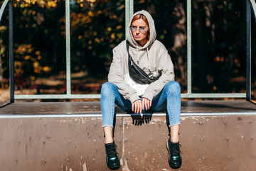 Stylish model girl at skate park in glasses with waist bag