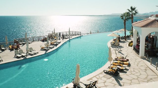 Timelapse of swimming pool at resort. Young girls relaxing on deck chairs. Luxury infinity pool with stunning views. Enjoying vacation at resort by sea. Sharm El Sheikh, Egypt 4k