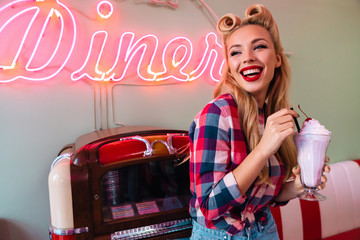 Photo of young cheerful woman drinking milkshake while leaning jukebox