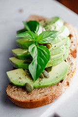 Avocado toast with pepitas and fresh basil on a white marble cutting board. Home cooking, healthy eating concept.
