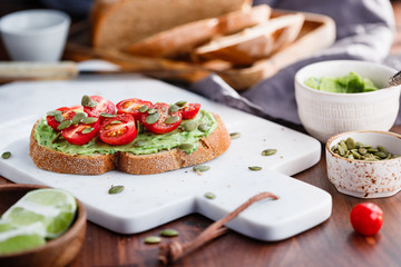 Avocado toast with cherry tomatoes and pepitas on a white marble cutting board. Home cooking, healthy eating concept.