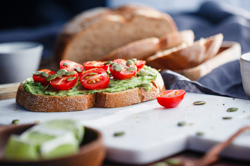 Avocado toast with cherry tomatoes and pepitas on a white marble cutting board. Home cooking, healthy eating concept.