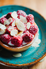 Raspberry tartlet dessert with almond flakes on a blue ceramic plate. Close-up view.