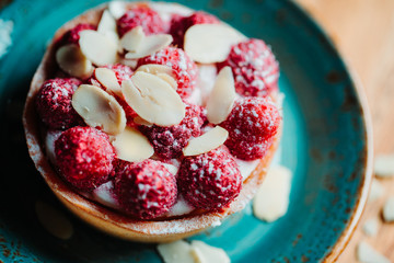 Raspberry tartlet dessert with almond flakes on a blue ceramic plate. Close-up view.