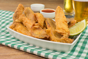 Fried Tilapia strips in platter with beer and sauces in wood background