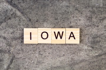 Iowa word written on wood block, on gray concrete background. Top view.