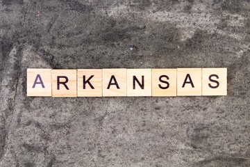 Arkansas word written on wood block, on gray concrete background. Top view.