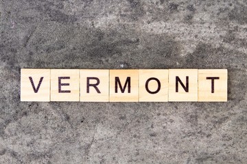 Vermont word written on wood block, on gray concrete background. Top view.