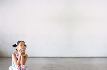 Asian child cute or kid girl thinking sit for new idea and imagination or creative education with vacant smile on street or kindergarten nursery preschool and dirty white wall background with space