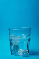 Close up of painkiller tablet in glass of water over blue background