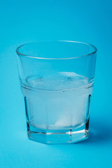 Close up of painkiller tablet in glass of water over blue background