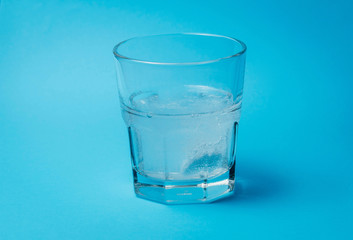 Close up of painkiller tablet in glass of water over blue background