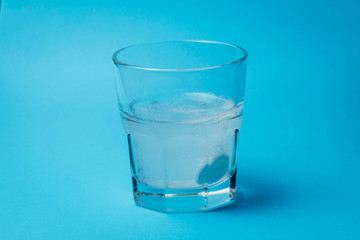 Close up of painkiller tablet in glass of water over blue background