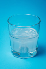 Close up of painkiller tablet in glass of water over blue background