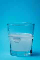 Close up of painkiller tablet in glass of water over blue background