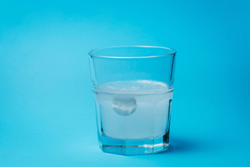 Close up of painkiller tablet in glass of water over blue background