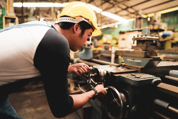 Sideway of an Asian industrial worker operating machine and concentrate working in a metal factory in a warm color tone with copy space, manufacturing industry concept, skilled profession occupation.