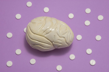 3D anatomical model of brain is on purple background surrounded by white pills as ornament polka dots. Medical concept by pharmacological tableted treat of brain and neurology disease pharmacotherapy