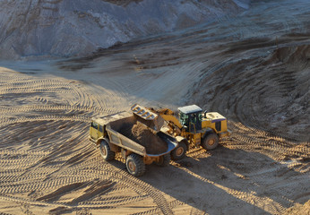 Wheel loader loads sand into heavy mining dump truck at the opencast mining quarry. Heavy machinery...