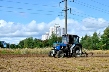 Blue tractor in a field of land plowing. Mechanization of tillage and crop planting. Loosening and...