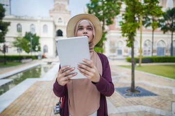 Portrait of beautiful young solo Muslim traveler exploring the city with viewing map on her tablet