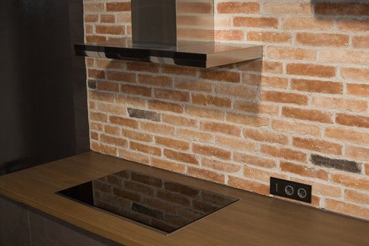 Modern kitchen with electric oven, electic stove and exhauster kitchen fan or range hood. Modern air Stainless steel chimney hood. Island hood against the background of a brick wal. Small sharpness