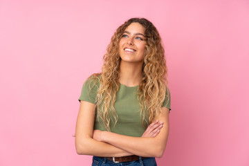 Young blonde woman with curly hair isolated on pink background looking up while smiling