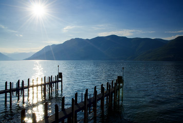 Pier with Sunbeam and Mountain on Alpine Lake Maggiore in Ticino, Switzerland.
