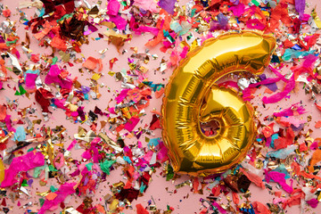Number 6 gold birthday celebration balloon on a confetti glitter background