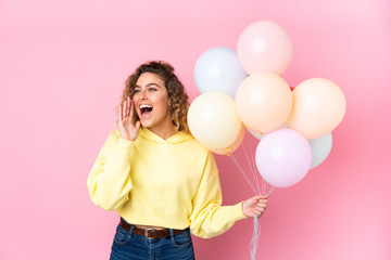 Fototapeta na wymiar Young blonde woman with curly hair catching many balloons isolated on pink background shouting with mouth wide open