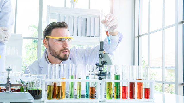 male scientist holding a tube with liquid substance. Man Research is working in the Laboratory with foreground of tube and Beaker of liquid substance.