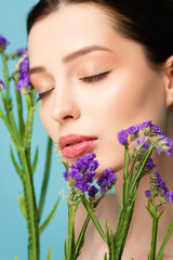 selective focus of naked woman with closed eyes near limonium flowers isolated on blue