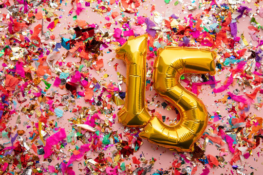 Number 15 gold birthday celebration balloon on a confetti glitter background
