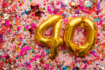 Number 40 gold birthday celebration balloon on a confetti glitter background