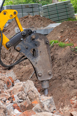 Excavator with hydraulic hammer breaker is crashing brick wall. Selective focus.