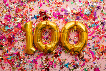 Number 100 gold birthday celebration balloon on a confetti glitter background