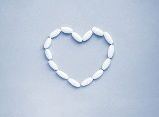 Heart shape made from pills for therapy, concept of treatment and health care on soft blue