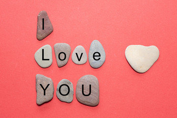 The message I love you stands as single letters on smooth natural stones with natural colors against a red background with a natural stone in the shape of a heart