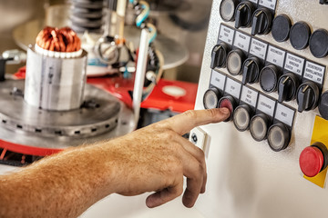 A hand pushes the stop button of a robot machine that winds and inserts the coils into the armature...