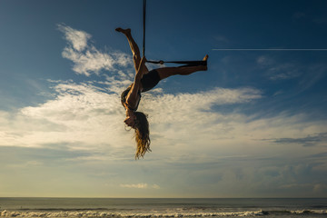 aero yoga beach workout - silhouette of young attractive and athletic woman practicing aerial yoga exercise training acrobatic  body postures on blue sky over sea