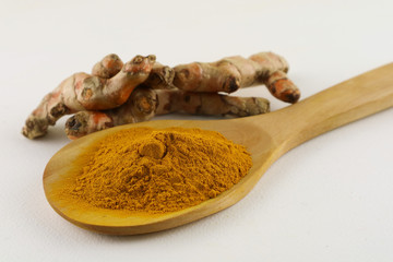 Turmeric powder in a spoon and turmeric root on a white background, used as a tonic for body and food ingredients.